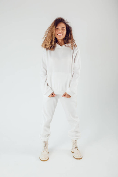 Attractive woman with thick curly hair in a white suit of hoodies and sweatpants. Mock-up. - Φωτογραφία, εικόνα