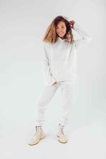Attractive woman with thick curly hair in a white suit of hoodies and sweatpants. Mock-up. - Fotó, kép