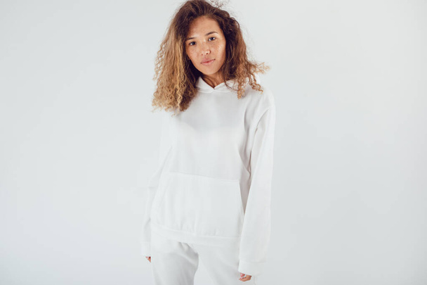 Attractive woman with thick curly hair in a white suit of hoodies and sweatpants. Mock-up. - Photo, image