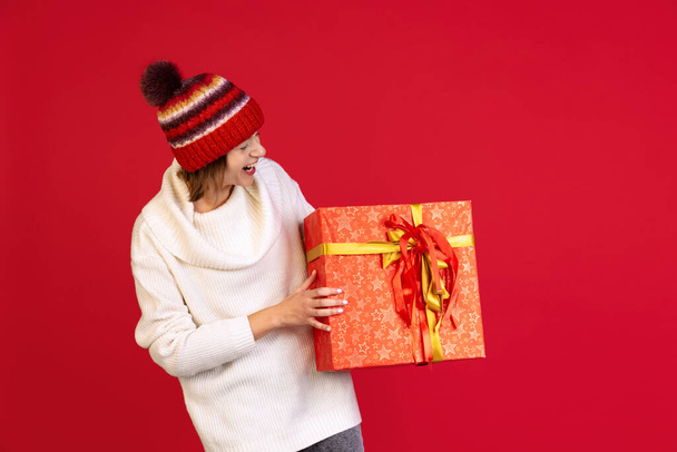 Cropped portrait of beautiful cheerful young woman with big present box posing isolated over red background. Holidays - Zdjęcie, obraz