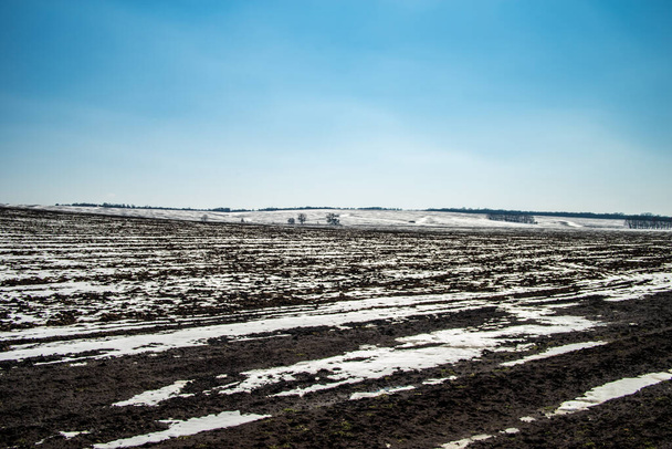 青い空に向かって丘の上の雪に覆われた畑。早春だ。選択的焦点. - 写真・画像