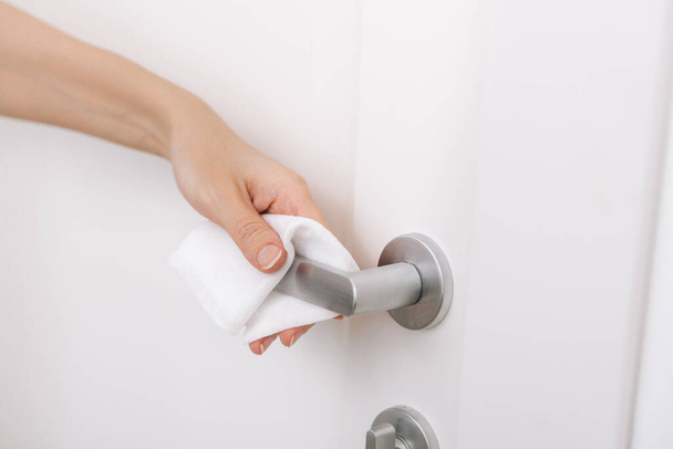 Cleaning door handles with an antiseptic wet wipe and gloves. Sanitize surfaces prevention in hospital and public spaces against corona virus. Woman hand using towel for cleaning home room door link - Photo, Image