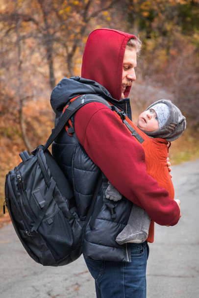 Mladý otec se svým dítětem v ergonomickém nosítkách na podzimní túře. Koncept nošení dětí a aktivního otce. - Fotografie, Obrázek
