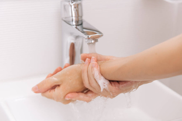 Washing hands under the flowing water tap. Hygiene concept hand detail. Washing hands rubbing with soap for corona virus prevention, hygiene to stop spreading corona virus in or public wash room - Zdjęcie, obraz