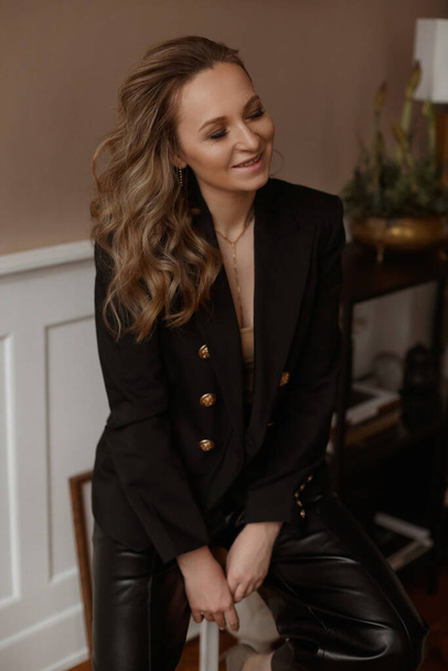 Charming woman with perfect trendy makeup and long wavy hair in an elegant suit posing in the interior. Adorable model girl with closed eyes in fashionable clothes - Photo, image
