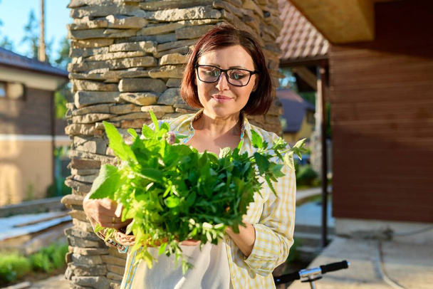 Woman in garden holding basket with freshly picked crop of green spicy fragrant herbs - Foto, Imagen