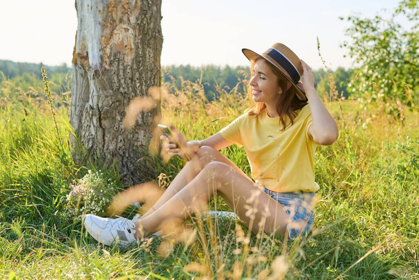 Glückliche erwachsene Frau sitzt auf der Wiese, ruht sich aus, benutzt Smartphone - Foto, Bild
