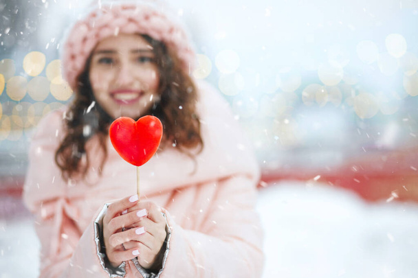 Mujer joven sonriente sosteniendo piruleta roja en forma de corazón. Espacio para texto - Foto, imagen