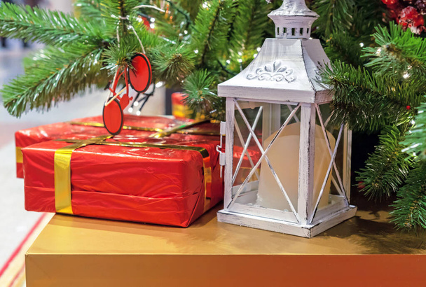 Witte lantaarn met een kaars en geschenken staan onder de kerstboom. - Foto, afbeelding