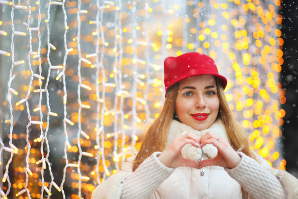 Όμορφη γυναίκα δείχνει καρδιά gymbol κατά bokeh φόντο. Κενό διάστημα - Φωτογραφία, εικόνα