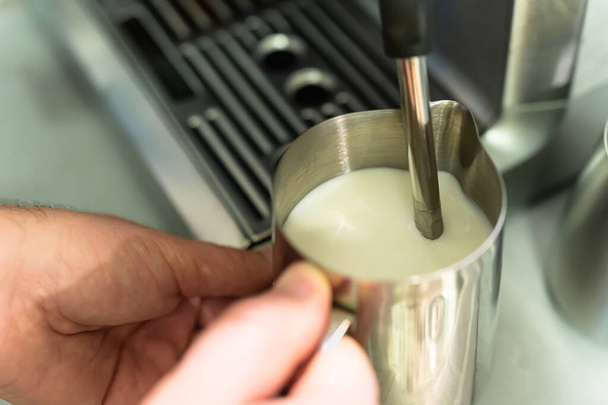 Ein Mann schäumt Milch für einen Cappuccino in einem Krug - Foto, Bild