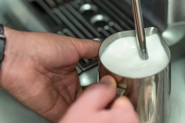 A man whisks milk for a latte in a steel jug - Photo, Image