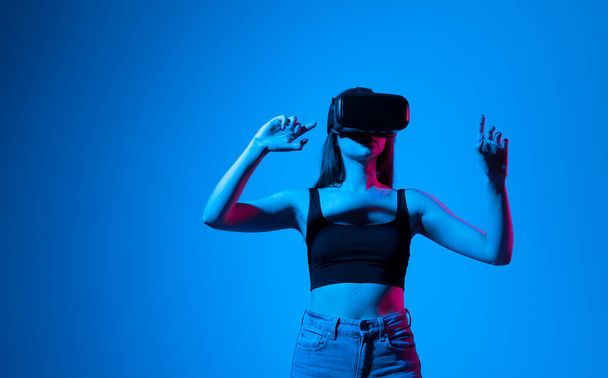 Young woman using the virtual reality headset and interact with a virtual world in a metaverse. Female model wearing VR goggles. - Fotó, kép