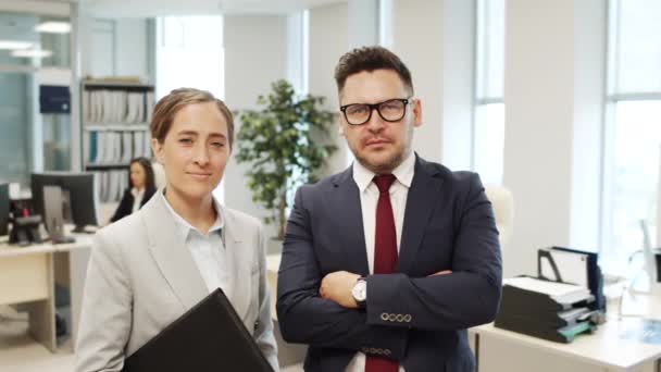 Portrait tracking shot of cheerful female personal assistant with clipboard and serious male CEO in suit posing for camera in office - Footage, Video