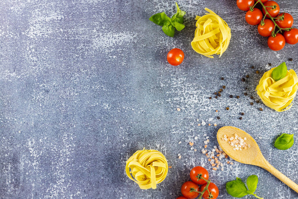 Italialaista pastaa. Litteä makasi harmaalla pohjalla ainesosista pastaa. Spagetti, kirsikkatomaatit, mausteet ja basilika. Tekstipaikka - Valokuva, kuva