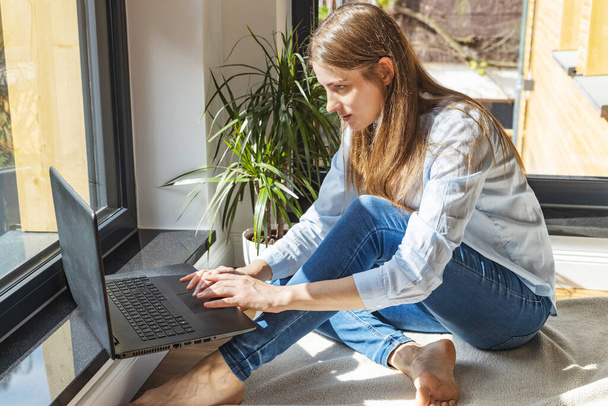 Een meisje zit op de vloer voor een laptop en koopt, kletst, studeert en zoekt informatie op het internet. Werk online. Freelance - Foto, afbeelding