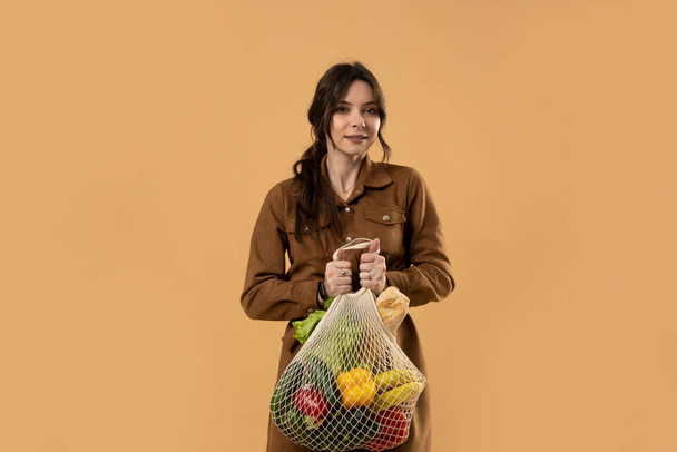 Zero waste concept. Young brunet woman holding reusable cotton shopping mesh bag with groceries from a market. Concept of no plastic. Zero waste, plastic free. Sustainable lifestyle. - Photo, Image