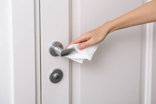 Cleaning door handles with an antiseptic wet wipe and gloves. Sanitize surfaces prevention in hospital and public spaces against corona virus. Woman hand using towel for cleaning home room door link - Φωτογραφία, εικόνα