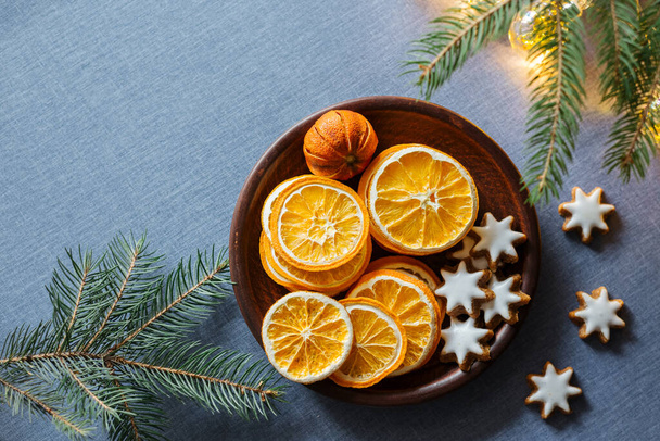 Winter background with dried oranges, ginger cookies pine tree branch and shiny garland on blue tablecloths. Top view, copy space - Photo, Image