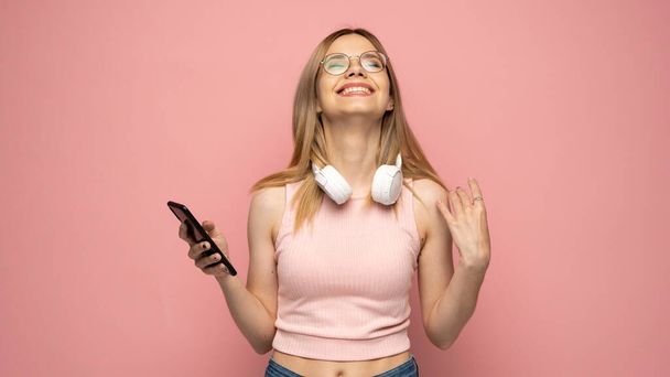 Closeup photo of attractive positive laughing young blonde woman wearing stylish yellow shirt and glasses communicating on mobile phone and smiling isolated over yellow background. - 写真・画像