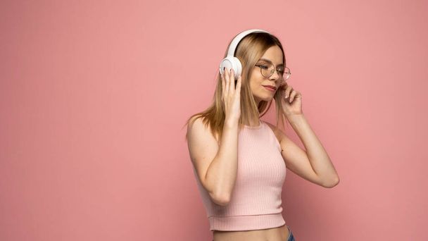 Happy girl in a glasses and pink shirt dancing and listening to the music isolated on a pink background. - Fotoğraf, Görsel