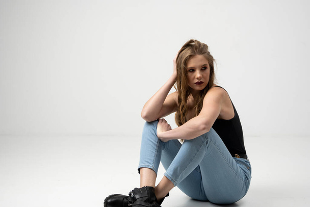 Beautiful young woman portrait in a black t-shirt and blue jeans. Studio shot, isolated on gray background. - Valokuva, kuva