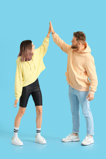 Cool mladý pár v mikinách dávat navzájem high-five na barevném pozadí - Fotografie, Obrázek
