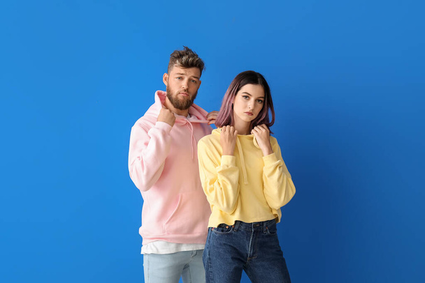 Cool pareja joven en sudaderas con capucha sobre fondo de color - Foto, imagen