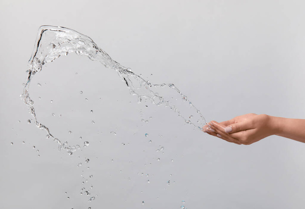 Female hands and splash of water on light background - Foto, afbeelding