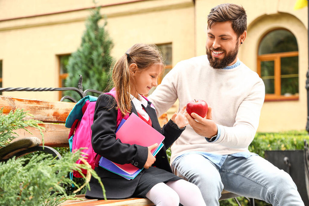 Человек дает своей маленькой дочери яблоко перед школой - Фото, изображение