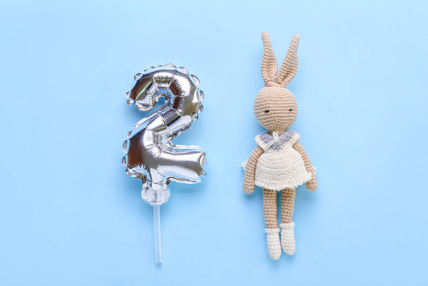 Silver balloon in shape of figure 2 and toy rabbit on blue background - Photo, Image