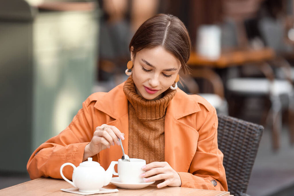 Beautiful woman stirring tea in street cafe - Photo, Image