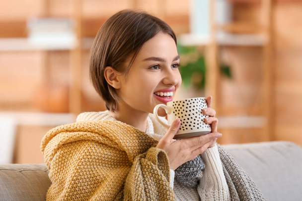 Beautiful young woman drinking tasty tea on sofa at home - Фото, изображение