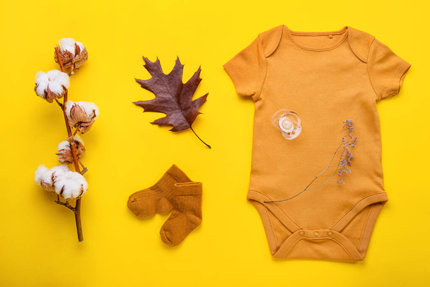 Composición con ropa de bebé, chupete y rama de algodón sobre fondo de color - Foto, Imagen