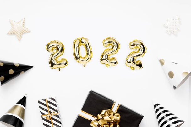 Happy New year 2022 celebration card. Gold foil balloons numeral 2022 on white background. Gifts and party hats. - Fotoğraf, Görsel