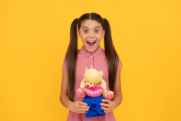 niesamowite nastolatek dziewczyna trzymać niedźwiedź zabawki i pudełko na żółtym tle, boks dzień - Zdjęcie, obraz
