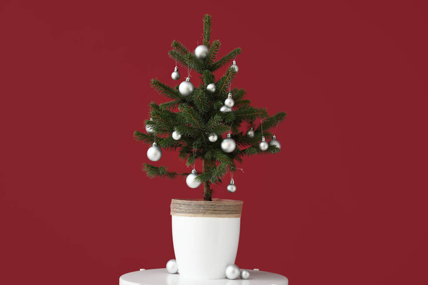 Όμορφο διακοσμημένο χριστουγεννιάτικο δέντρο σε κατσαρόλα στο τραπέζι κοντά στον κόκκινο τοίχο - Φωτογραφία, εικόνα