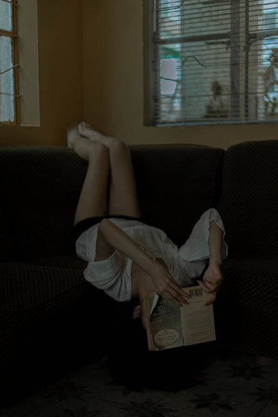 young woman sitting on sofa and reading book - Fotografie, Obrázek
