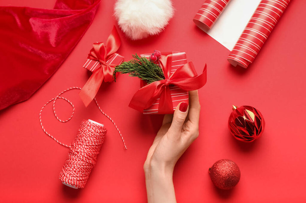 Женская рука с рождественскими подарками, веревкой и украшениями на цветном фоне - Фото, изображение