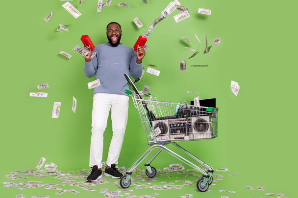 Photo of funky african guy dressed grey sweater spending dollars modern gadgets isolated green color background - 写真・画像