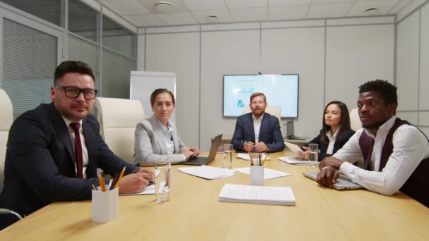 Фотография бизнесменов, сидящих за столом в конференц-зале и смотрящих в камеру во время обсуждения работы - Кадры, видео