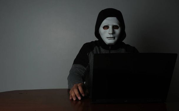 A low exposure picture of hacker with laptop insight. Hacking and cyber security threat concept. - Photo, Image