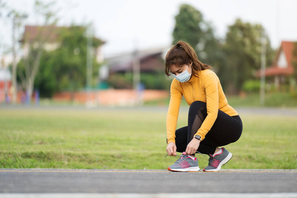 young woman tying her running shoes and wearing medical mask to protect Coronavirus(Covid-19) pandemi - Foto, Imagem