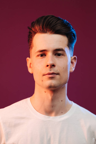 Close up portrait of serious handsome guy in white t-shirt isolated on crimson background - Zdjęcie, obraz