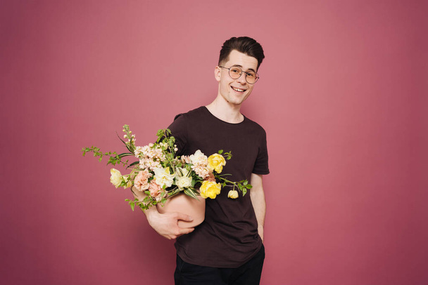 Χαρούμενος όμορφος νεαρός που κρατάει ένα μπουκέτο λουλούδια.. - Φωτογραφία, εικόνα