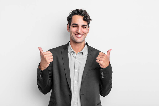 young businessman smiling joyfully and looking happy, feeling carefree and positive with both thumbs up - Photo, Image