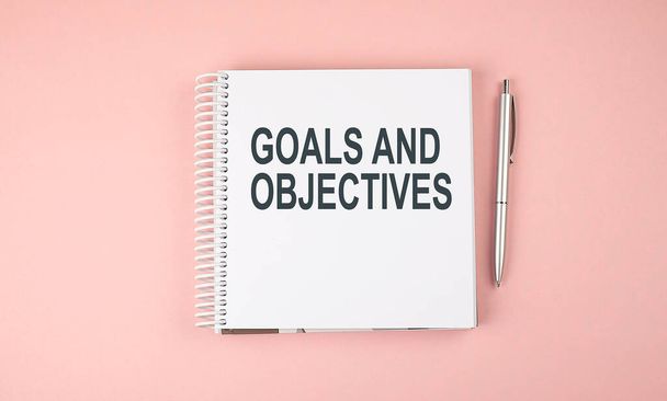 GOALS AND OBJECTIVES text on the notebook with pen on the pink background - Photo, Image