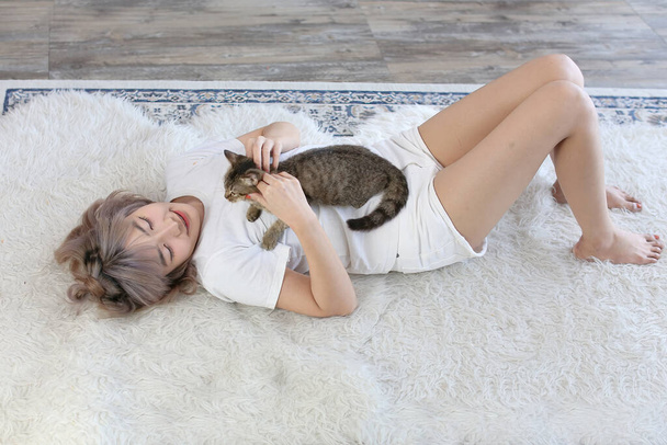 Молода азіатка грає з кішкою на килимі в вітальні.. - Фото, зображення
