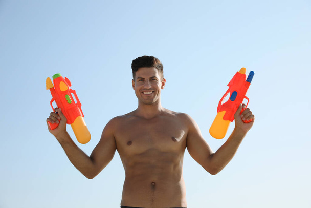 Man with water guns against blue sky - 写真・画像
