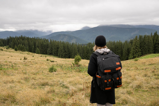 vista trasera de una mujer turista con una mochila, un viajero en las montañas mirando el paisaje, viajar a través de las montañas de Rumania, las montañas del Cáucaso en la niebla. Concepto de turismo de montaña - Foto, Imagen
